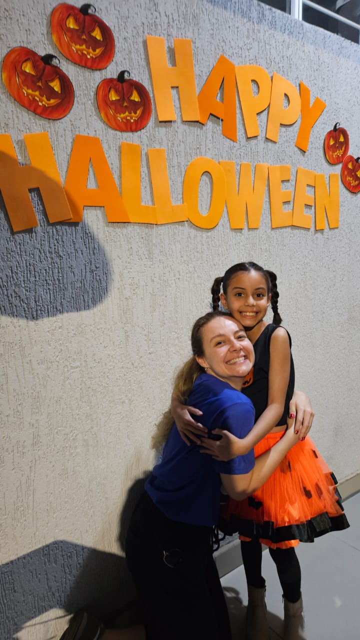 Professora abraçando aluna fantasiada no mural de Happy Halloween
