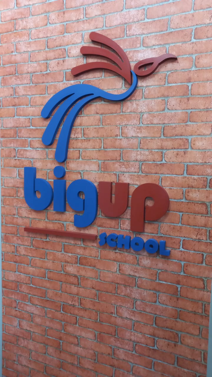Logotipo da BigUp School aplicado em relevo na parede de tijolos da escola