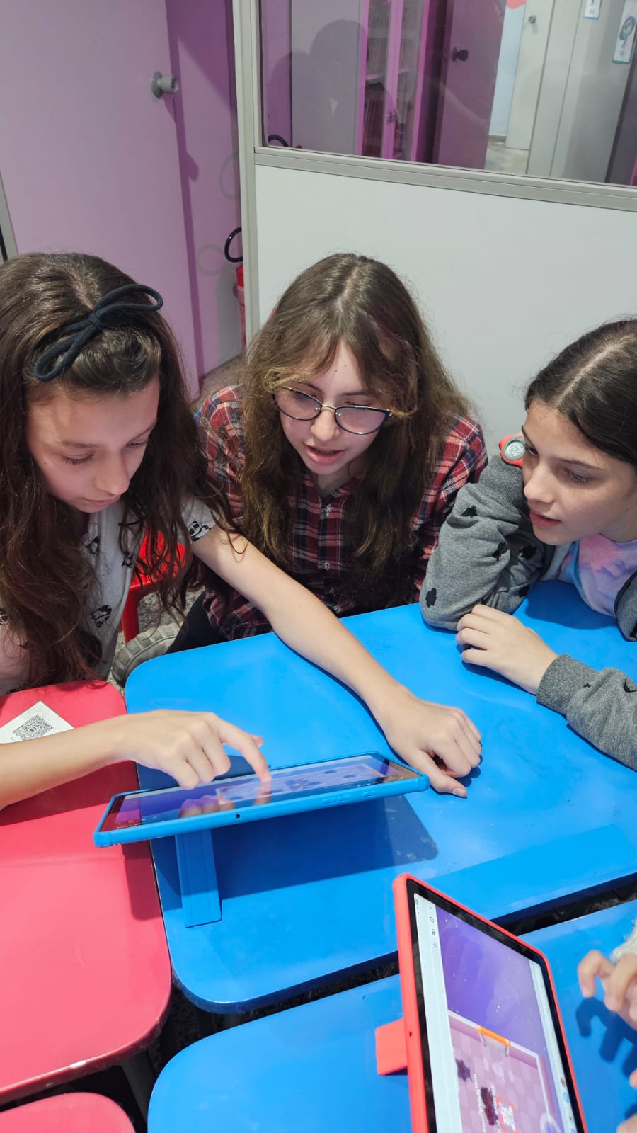 Três alunas usando um tablet em atividade de inglês na BigUp School